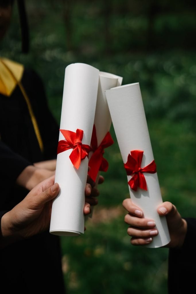 Three diplomas with red ribbons symbolize graduation success outdoors.