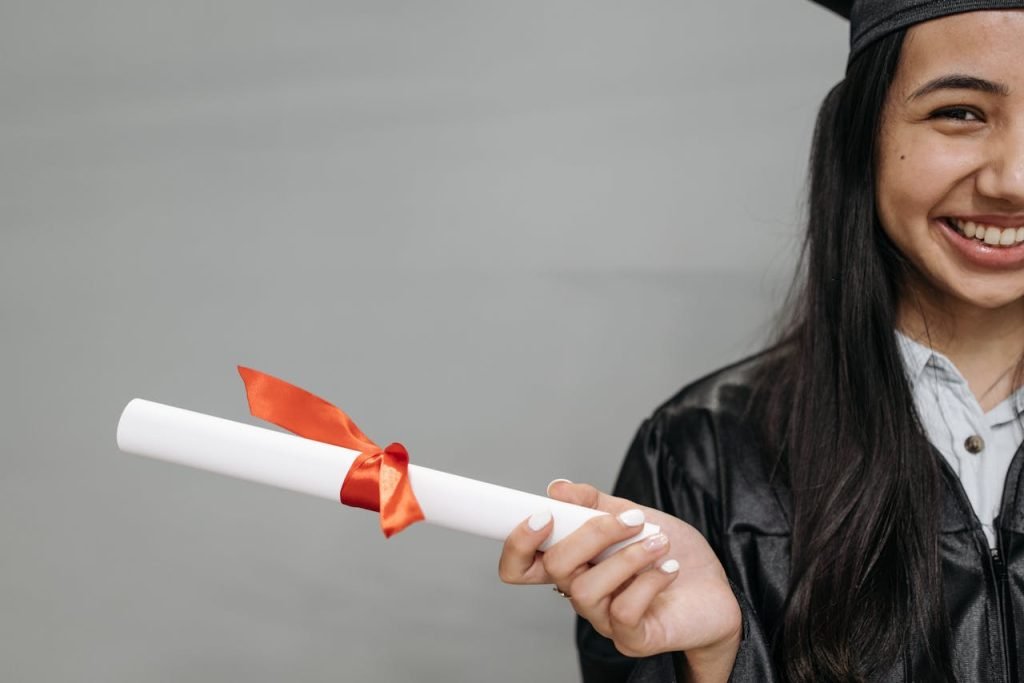 A happy female graduate smiles while holding a diploma tied with a red ribbon.